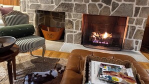 A stone fireplace with a fire, a green striped armchair, a brown leather sofa, and a dog.