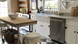 A kitchen with a checkered floor, white cabinets, a wooden table, and a stool.