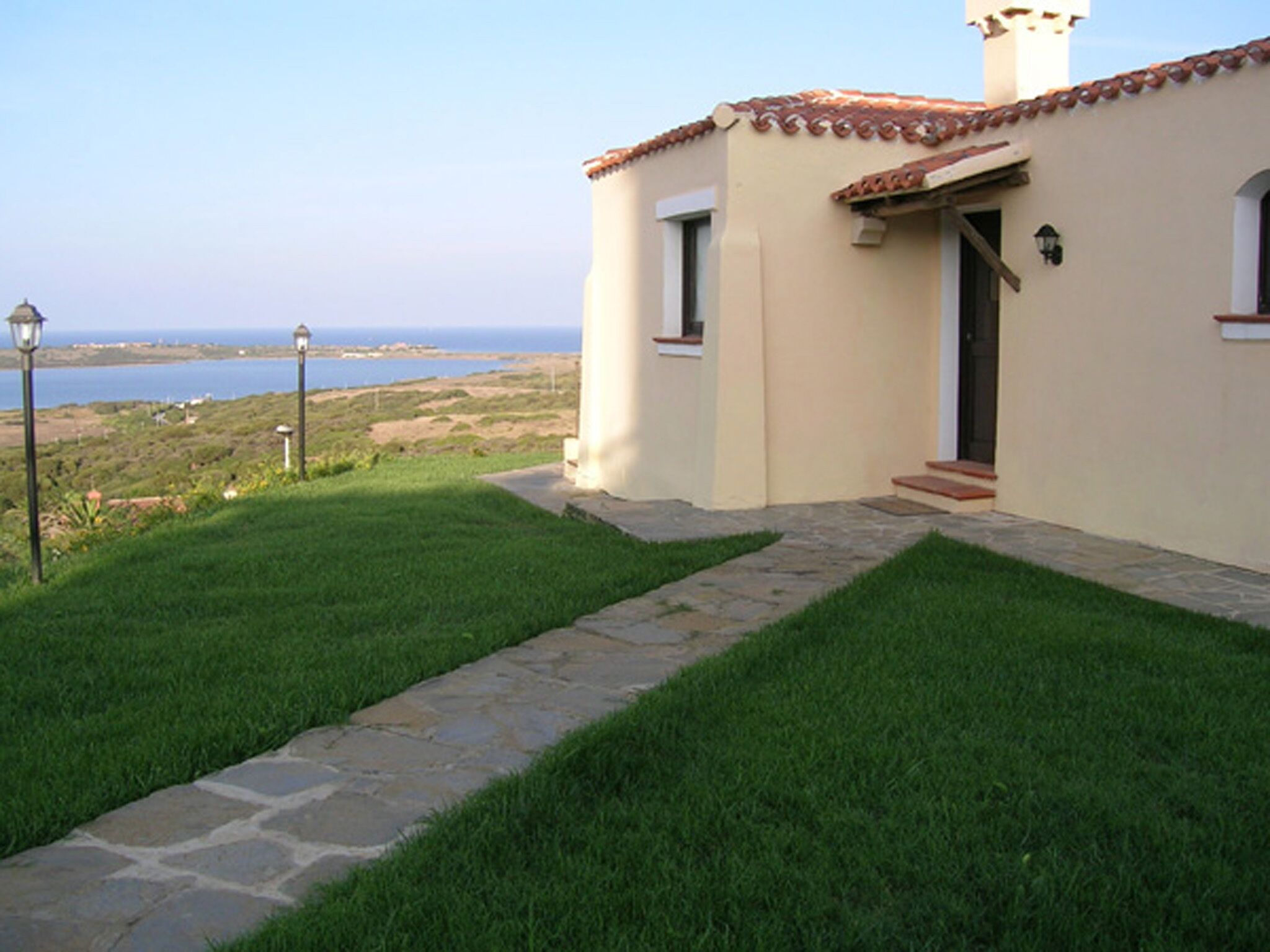 A house with a stone pathway leading to a door, a view of the ocean, and a lamp post in the foreground.