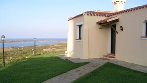 A house with a stone pathway leading to a door, a view of the ocean, and a lamp post in the foreground.