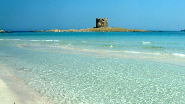 A clear beach with a small island featuring a single tower structure.