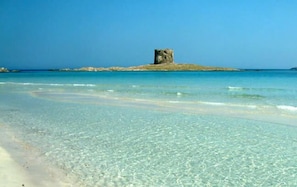 A clear beach with a small island featuring a single tower structure.