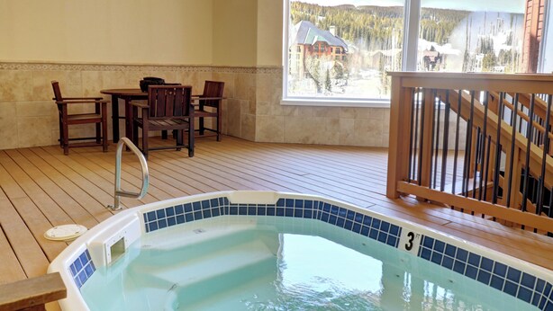 Una terraza de madera con un jacuzzi, una mesa y sillas.