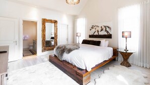 A bedroom with a large bed, a mirror, a painting, and a chandelier. - Tremblant Prestige - Panache 632 (Mont-Tremblant)