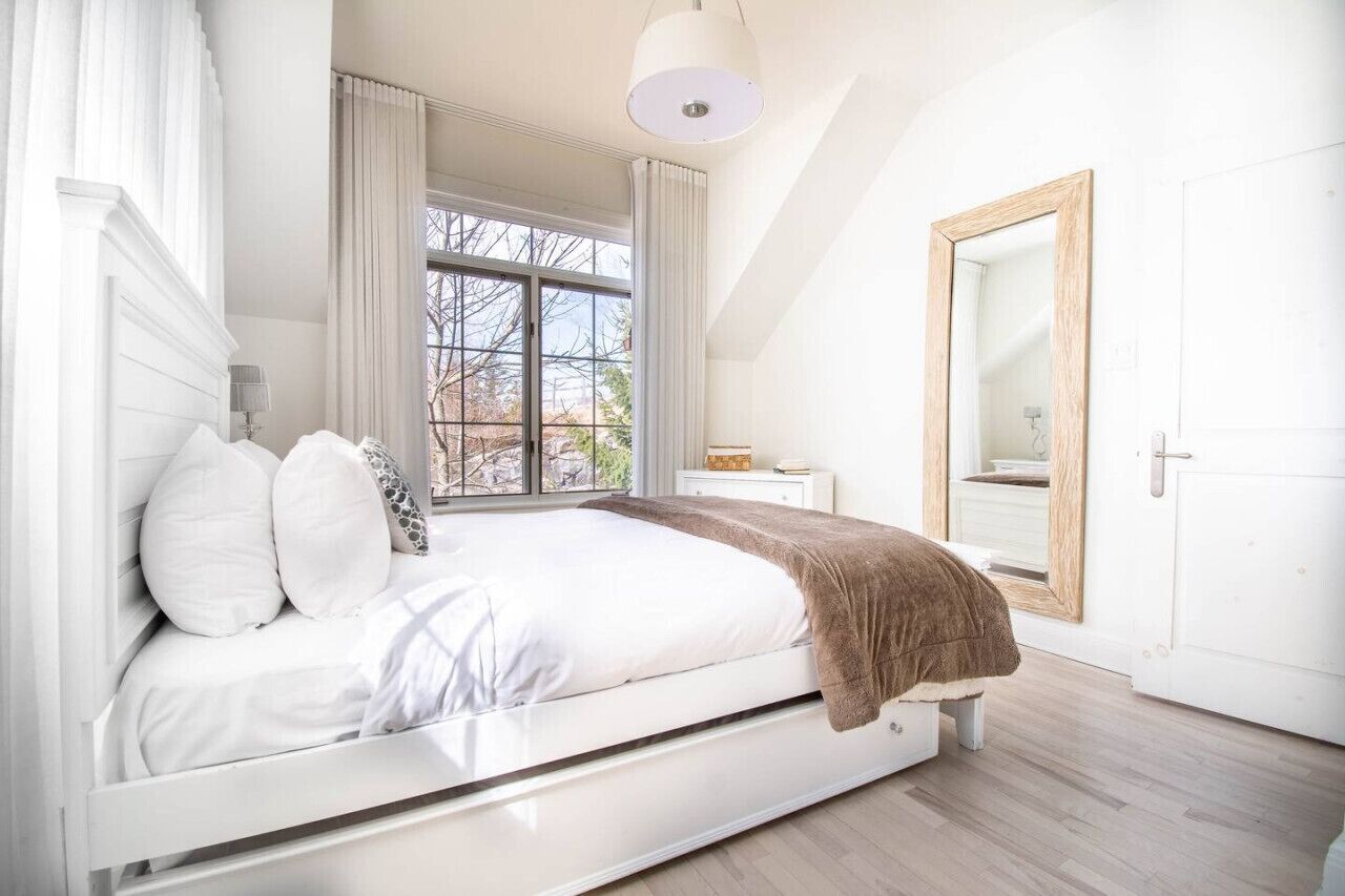 Un dormitorio con cama, ventana, espejo y puerta.