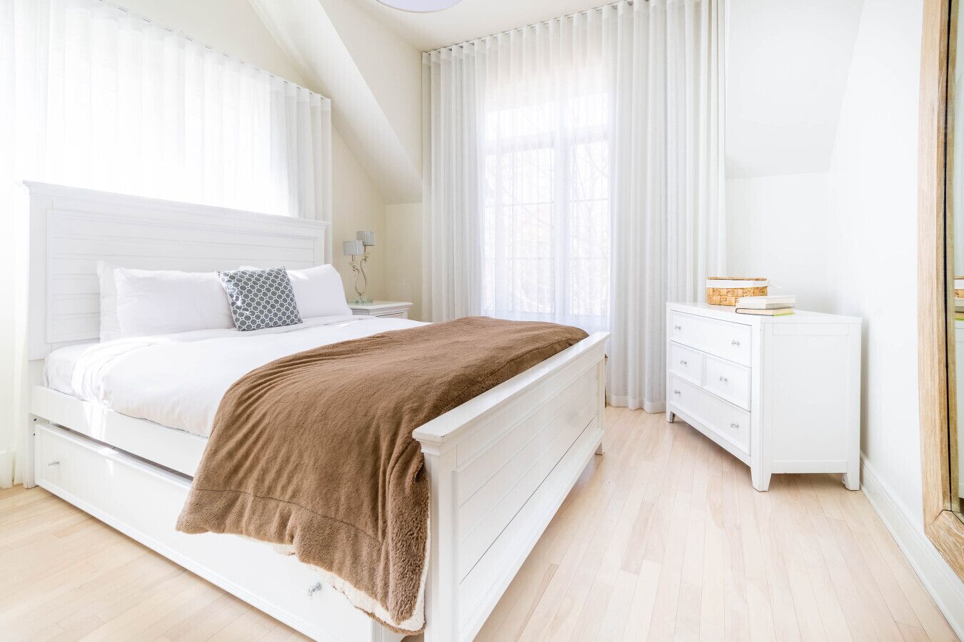 Ein Schlafzimmer mit einem Bett, Nachttischen in Weiß, einer Kommode und einem Fenster mit Vorhängen.