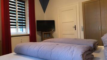 A bedroom with a bed, a television on a stand, a wardrobe, and a window with blinds.