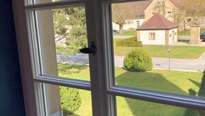 A window with a view of a well-maintained lawn, a small building, and a clear sky. - Appartements am Rindhof (Muennerstadt)