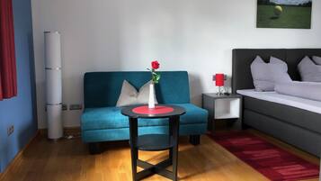 Ein modernes Zimmer mit einem blauen Sofa, einem kleinen runden Tisch mit einer Vase mit einer roten Rose, einem grauen Bett und einem roten Teppich.