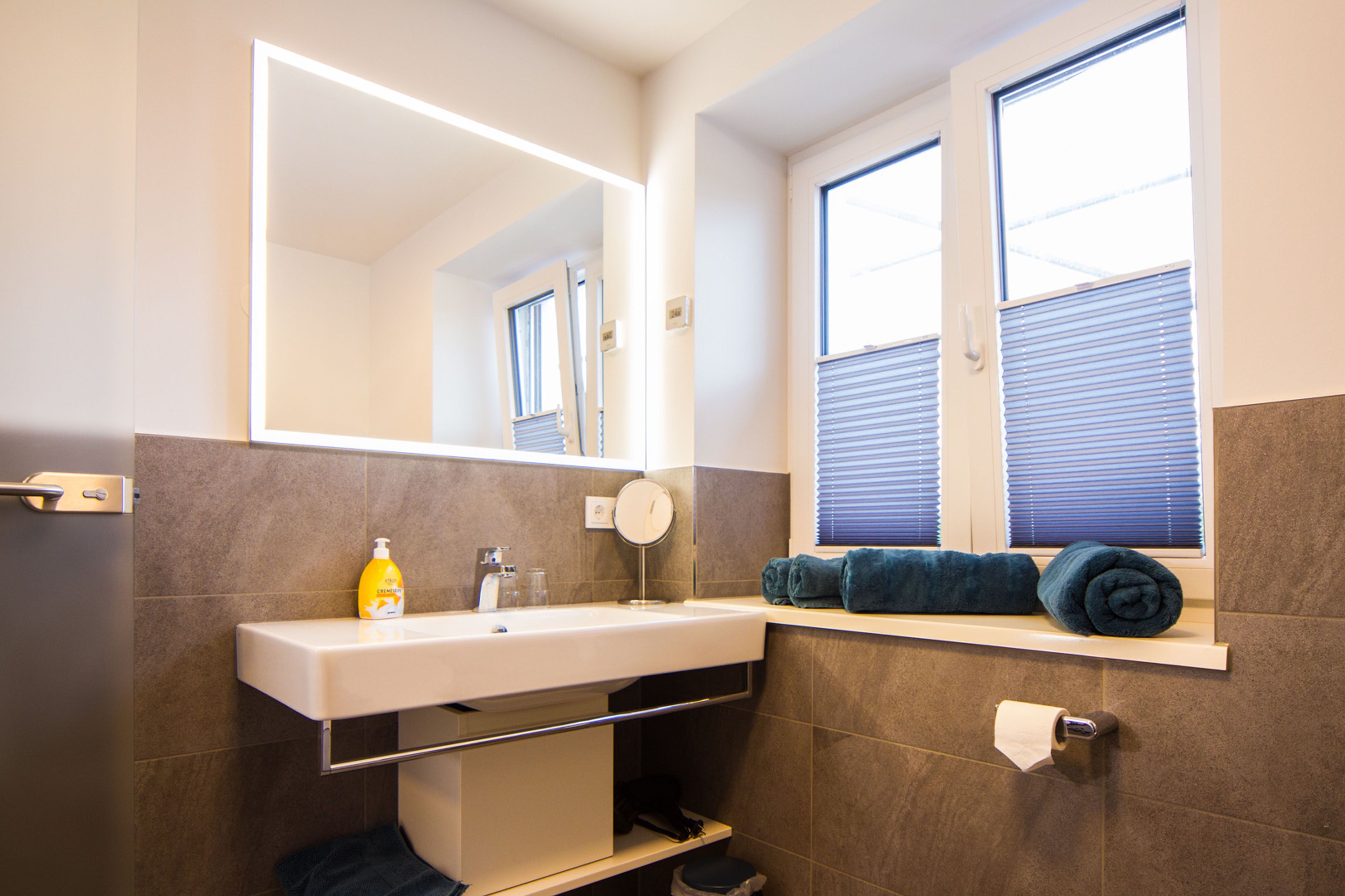 A bathroom with a sink, mirror, towel rack, and toilet paper.