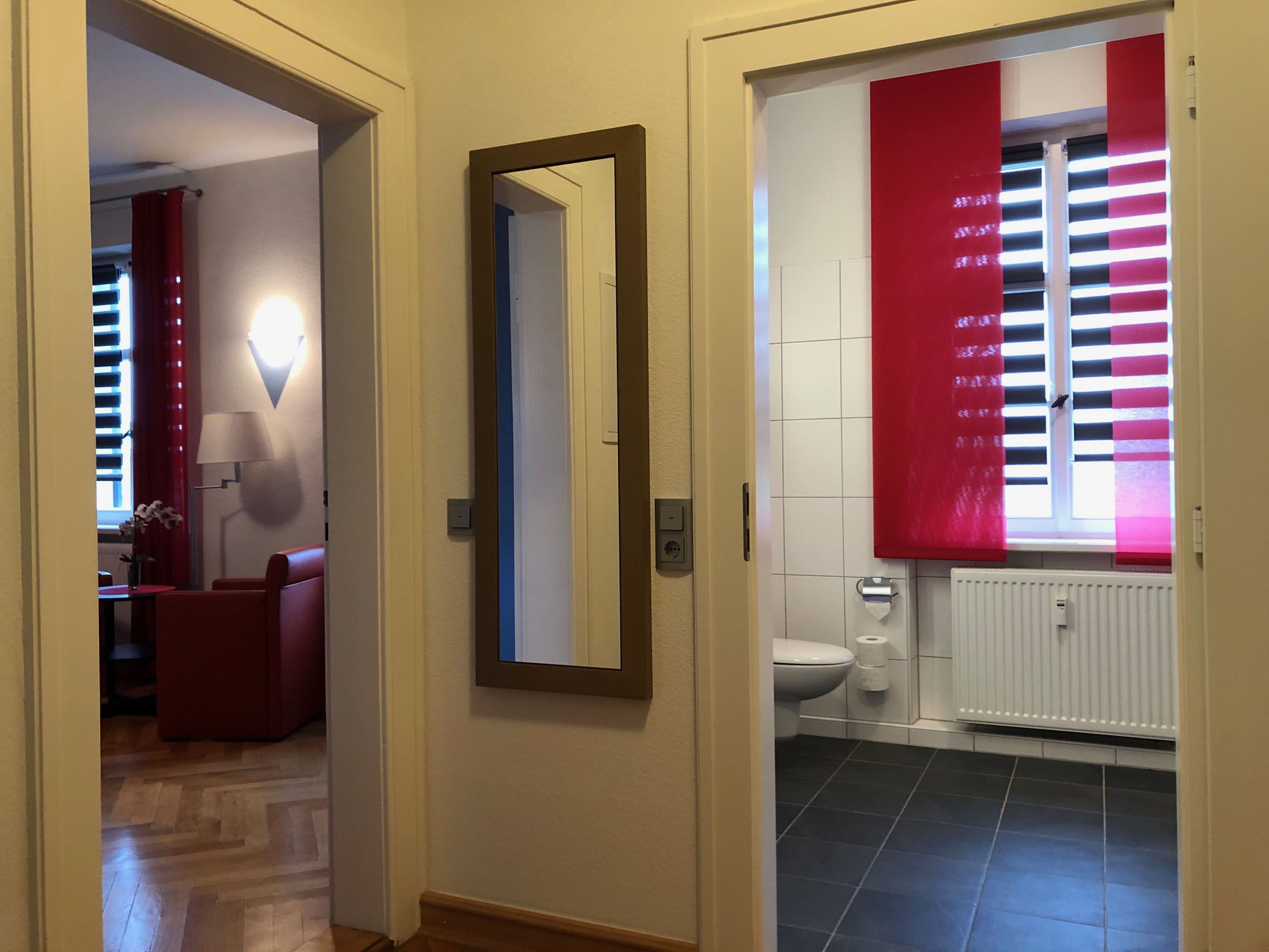 A hallway leading to a bathroom with a toilet, a mirror, and a red curtain.