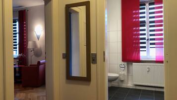 A hallway leading to a bathroom with a toilet, a mirror, and a red curtain.