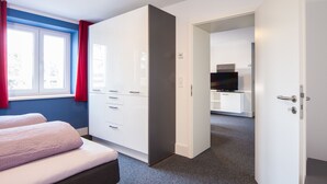 A hotel room with a bed, a wardrobe, a desk with a television, and a bathroom visible through an open door. - Appartements am Rindhof (Muennerstadt)