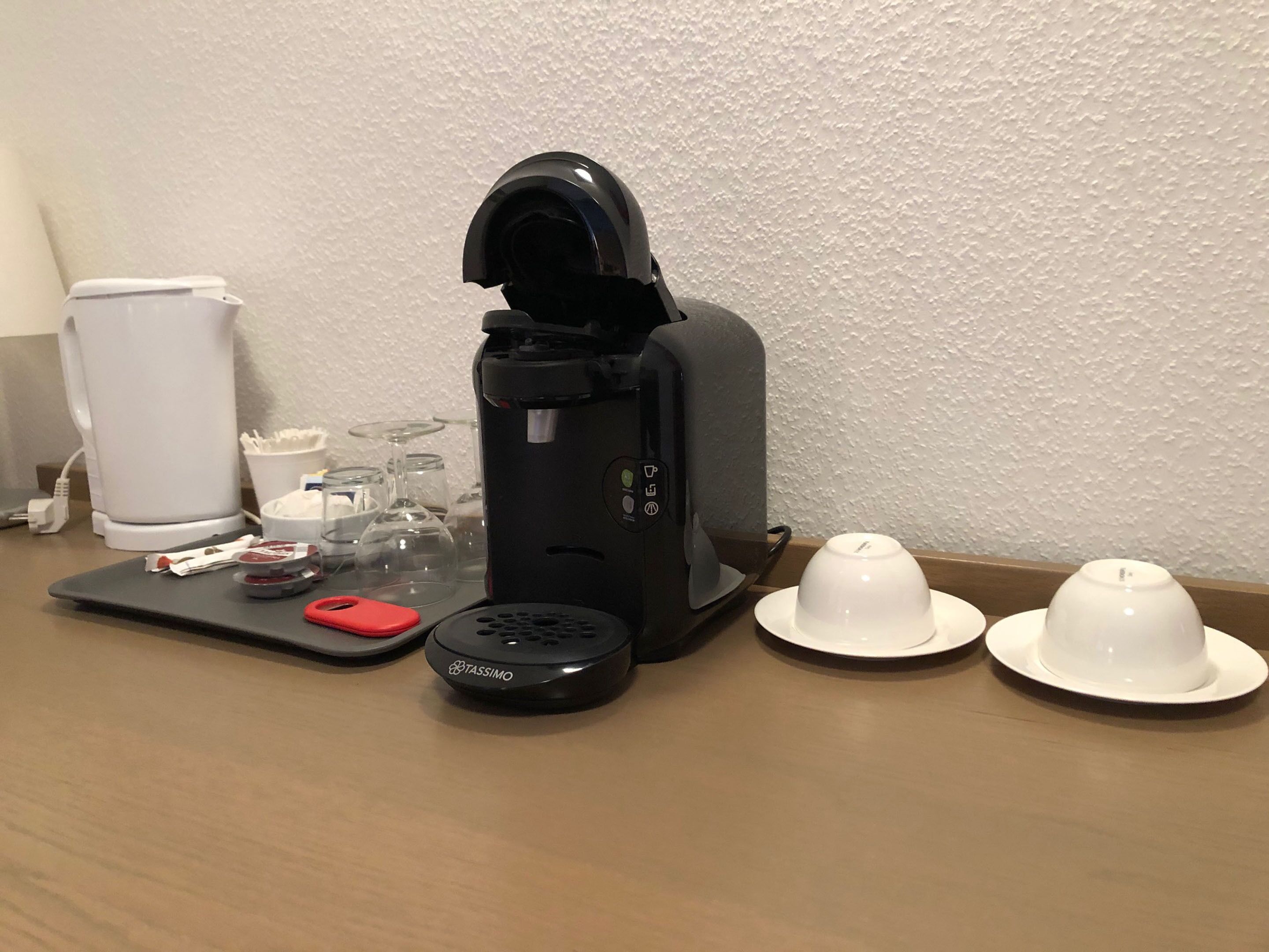 A coffee machine, a white cup, and two white hats on a table.