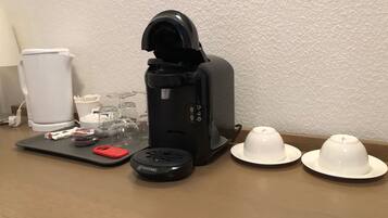 A coffee machine, a white cup, and two white hats on a table.