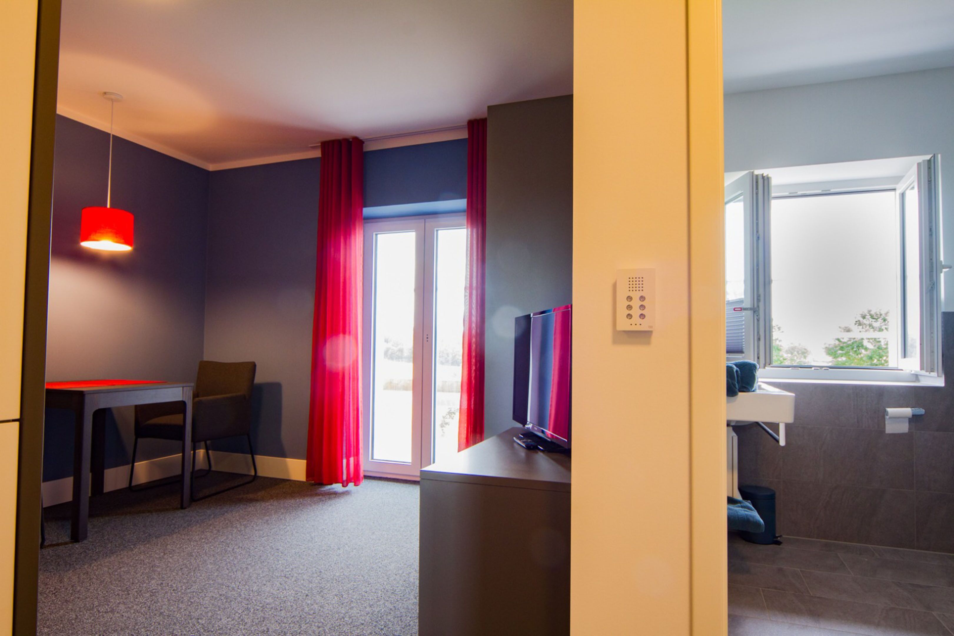 A hotel room with a desk, chair, TV, and a window with curtains.
