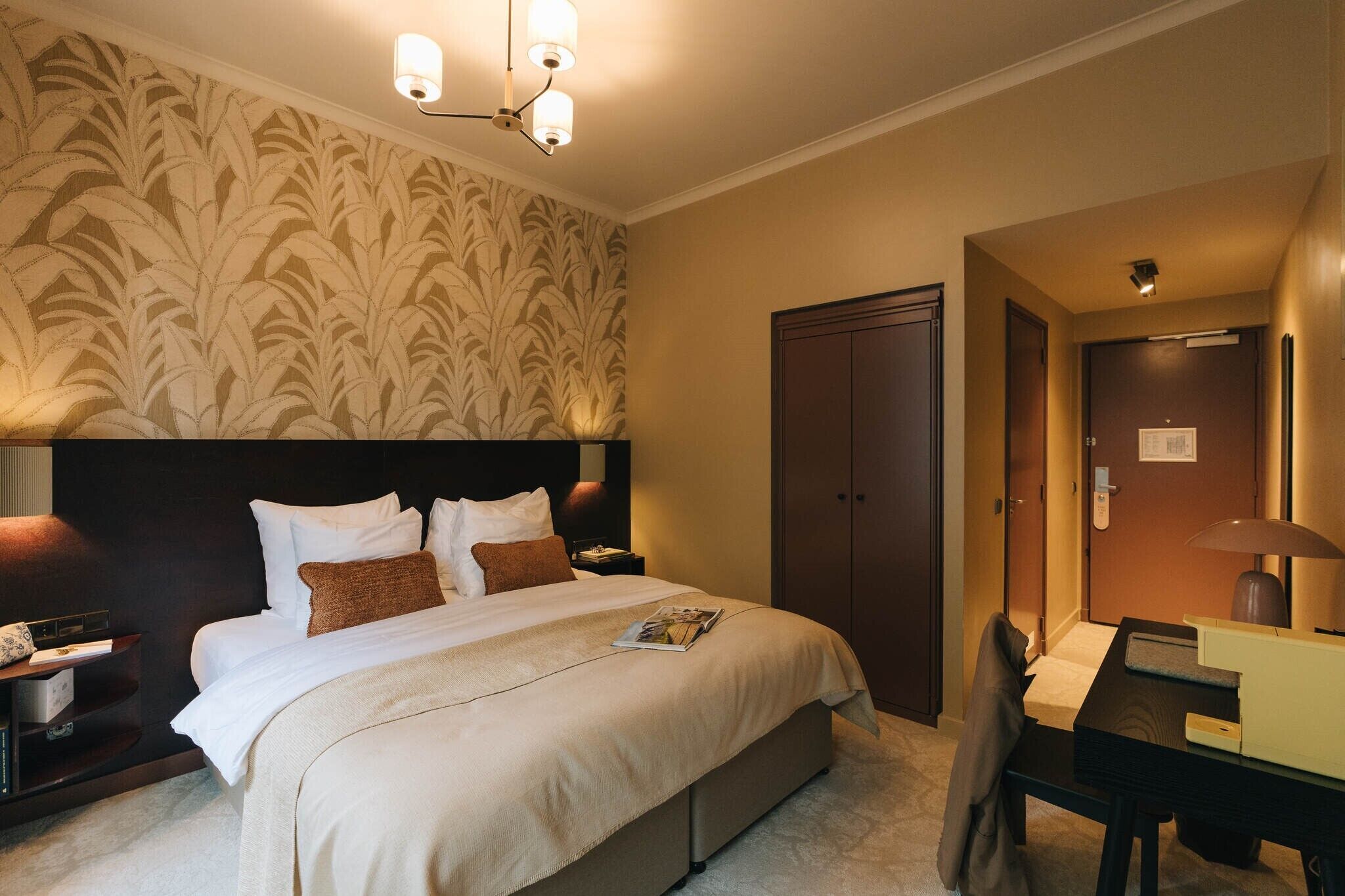 Habitación de hotel con una cama grande, un escritorio, una silla, un armario y una pared con un diseño de hojas.