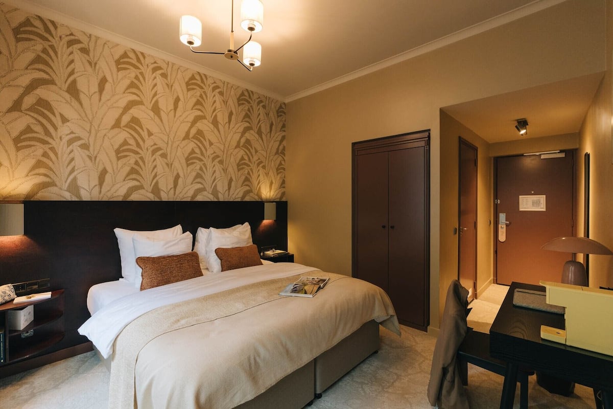 Habitación de hotel con una cama grande, un escritorio, una silla, un armario y una pared con un diseño de hojas.