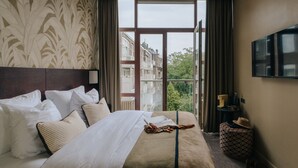 Un cuarto de hotel con una cama grande, un televisor montado en la pared y vistas de edificios a través de la ventana.