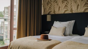 Una habitación de hotel con una cama grande, una mesita de noche y un ventanal con cortinas.
