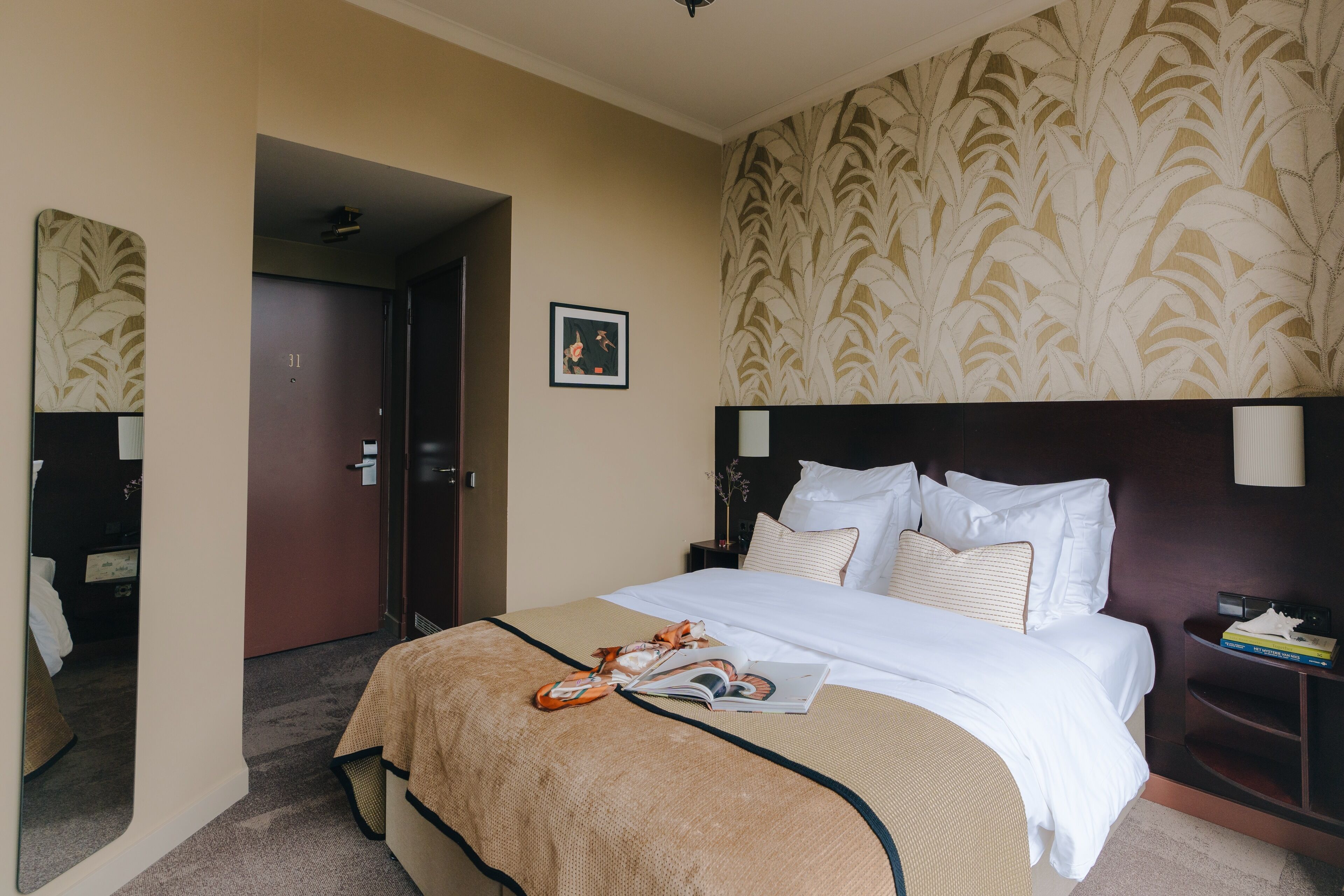 Ein Hotelzimmer mit einem großen Bett, einem Nachttisch, einem Spiegel und einer Tür zu einem anderen Raum.