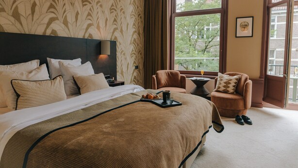 Habitación de hotel con una cama grande, una silla, una mesita y una ventana con vista a árboles.