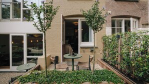 Un patio con una mesa y sillas, un edificio de ladrillo y un jardín con plantas.