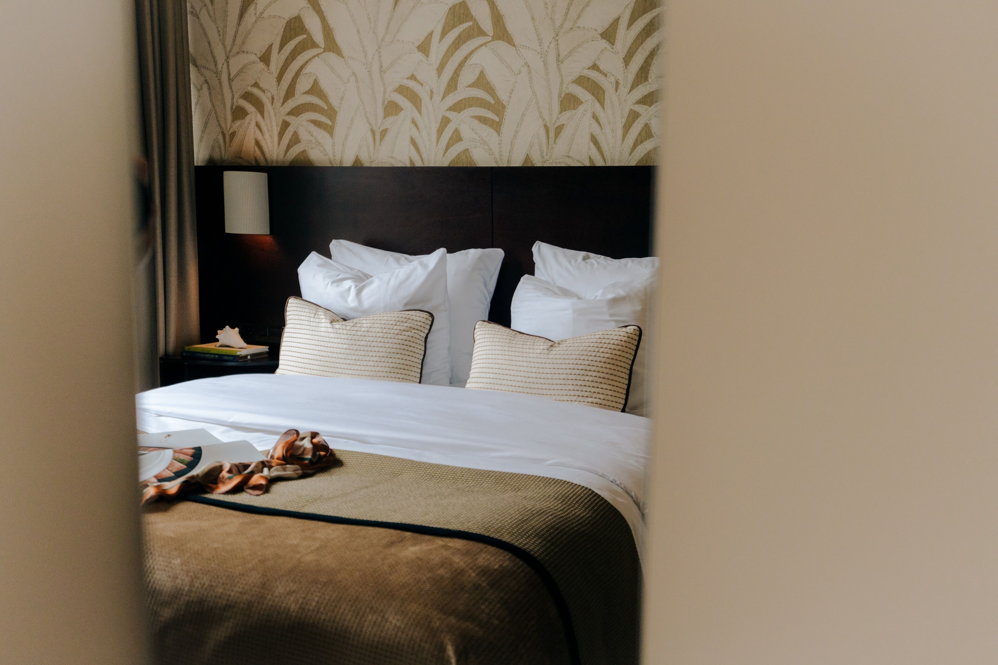 A hotel room with a large bed, two pillows, a nightstand, and a lamp.