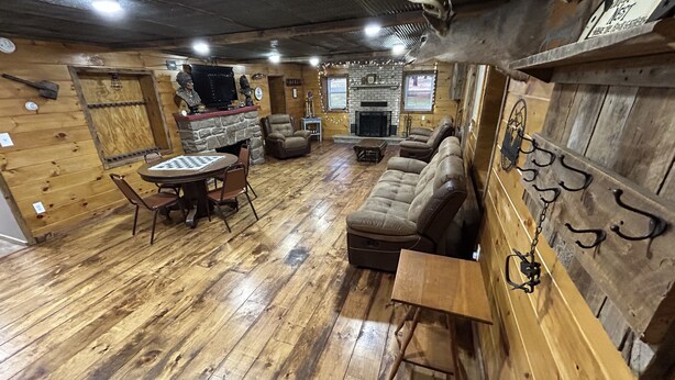 A rustic interior with wooden walls, a stone fireplace, leather sofas, and a dining area with a table and chairs. - Rustic Lodge near Black Moshannon & Penn State (Philipsburg)