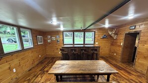 A rustic cabin interior with a wooden dining table, bar stools, and framed pictures on the walls. - Rustic Lodge near Black Moshannon & Penn State (Philipsburg)