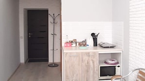 Un espacio habitable compacto con kitchenette, una puerta que da a una habitación oscura y una pared de ladrillo blanco.