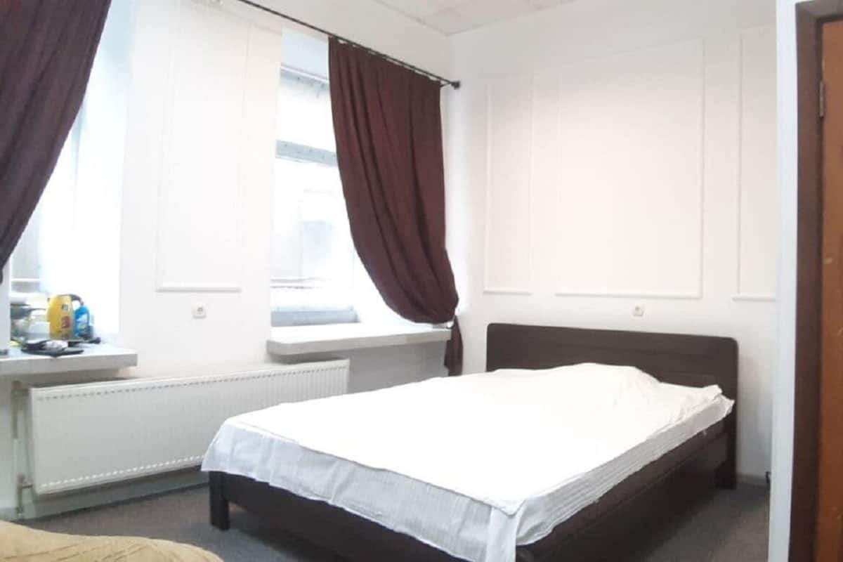 Un dormitorio con una cama individual, una ventana con cortinas, un radiador y una puerta de madera.