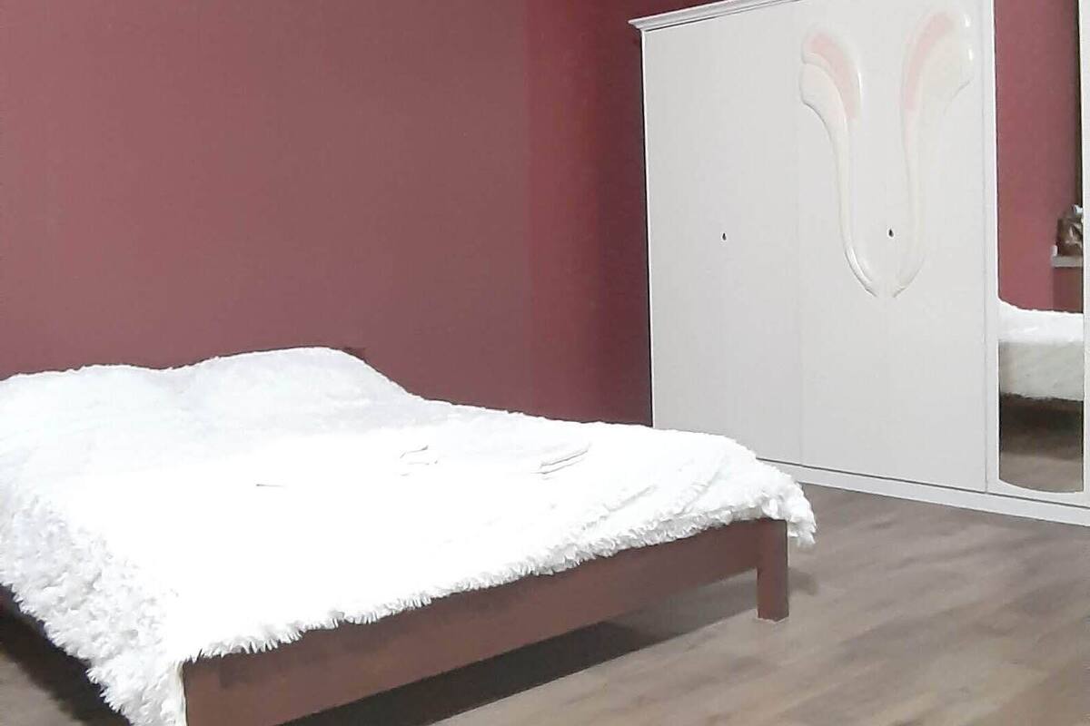 Un dormitorio con una cama de madera, un armario blanco y un espejo.