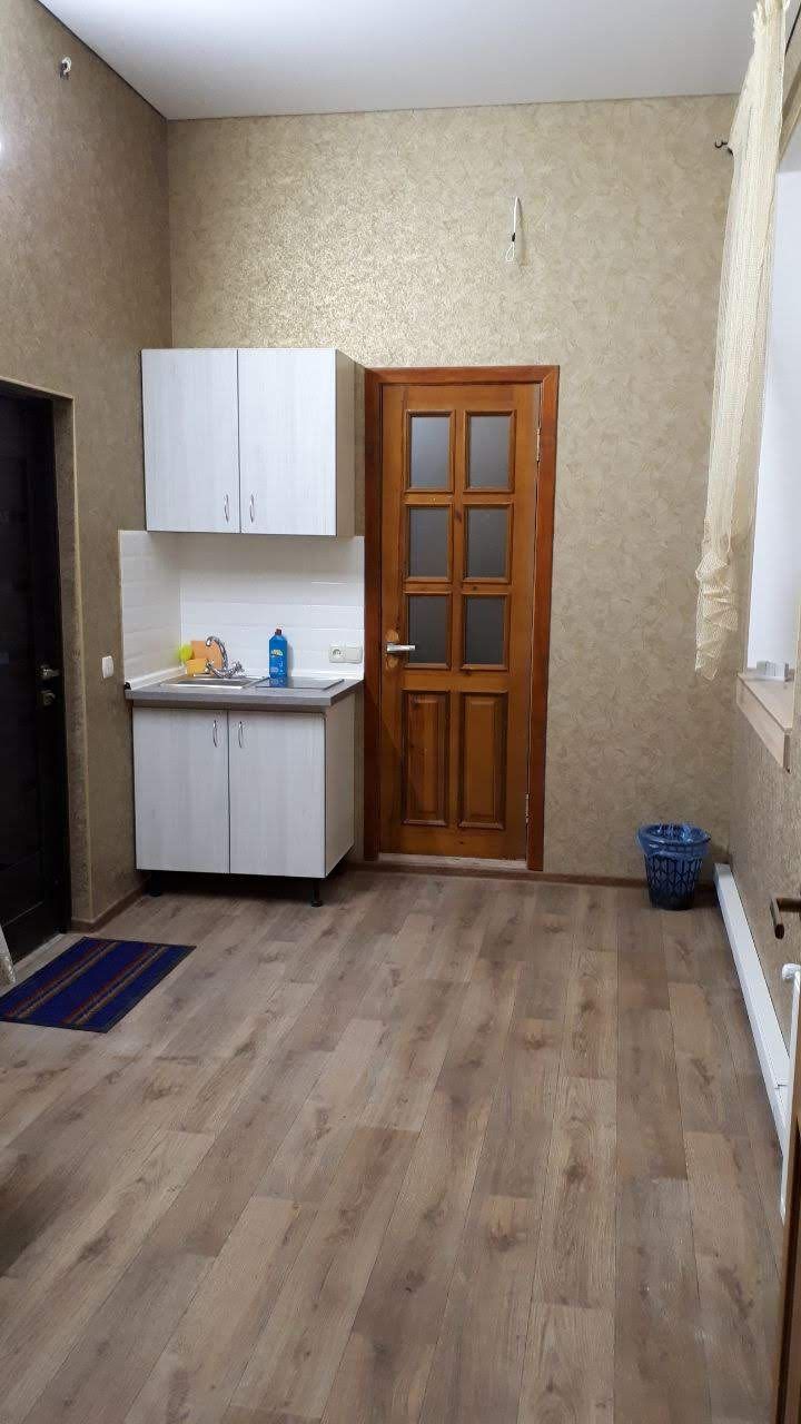 Una cocina compacta con armarios blancos, una puerta de madera y un cubo de basura azul.