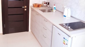 Cocina compacta con puerta de madera oscura, armarios blancos, un lavamanos, hervidor y lavavajillas.