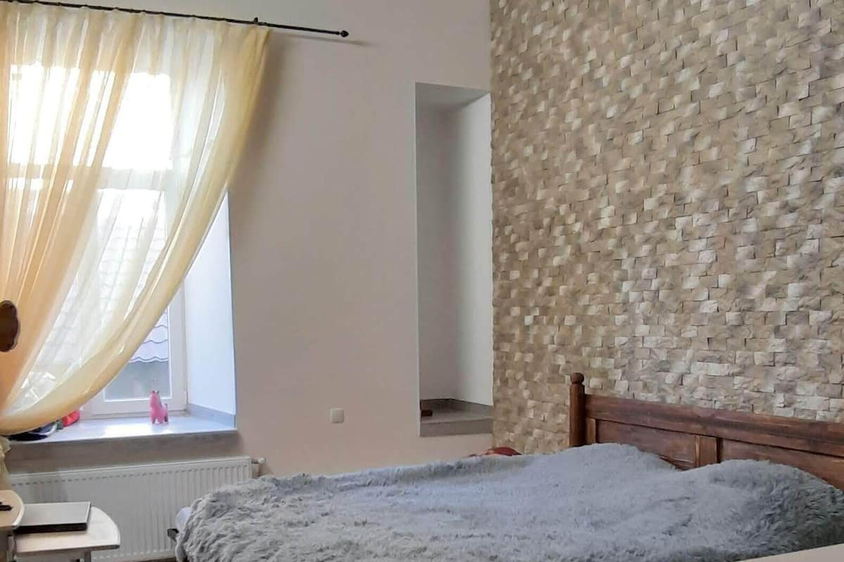 Un dormitorio con una cama de madera, un escritorio, una silla y una ventana con cortinas traslúcidas.