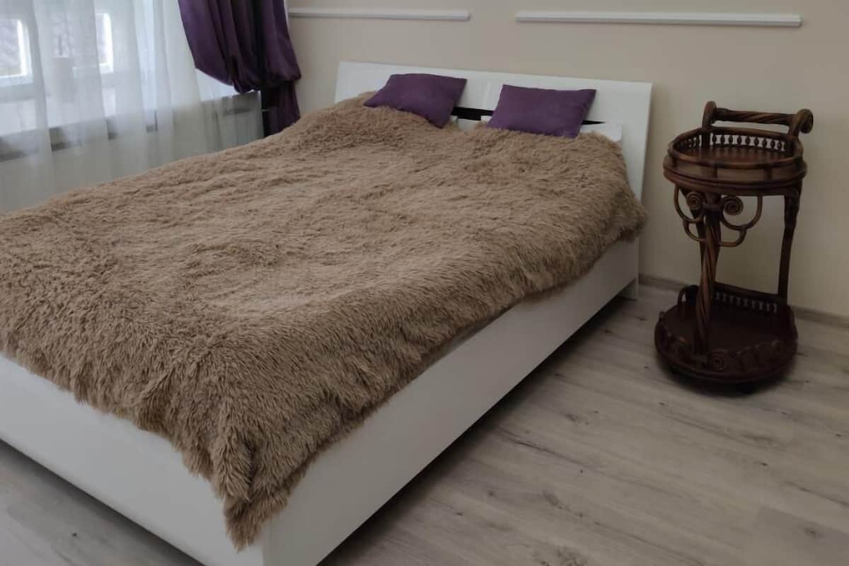 Un dormitorio moderno con una cama grande, una mesita de noche de madera y vistas al exterior a través de cortinas translúcidas.