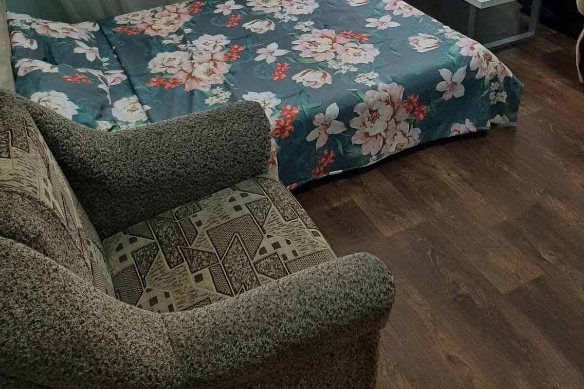 Un dormitorio con cama, una mesita, una silla y un televisor en la pared.