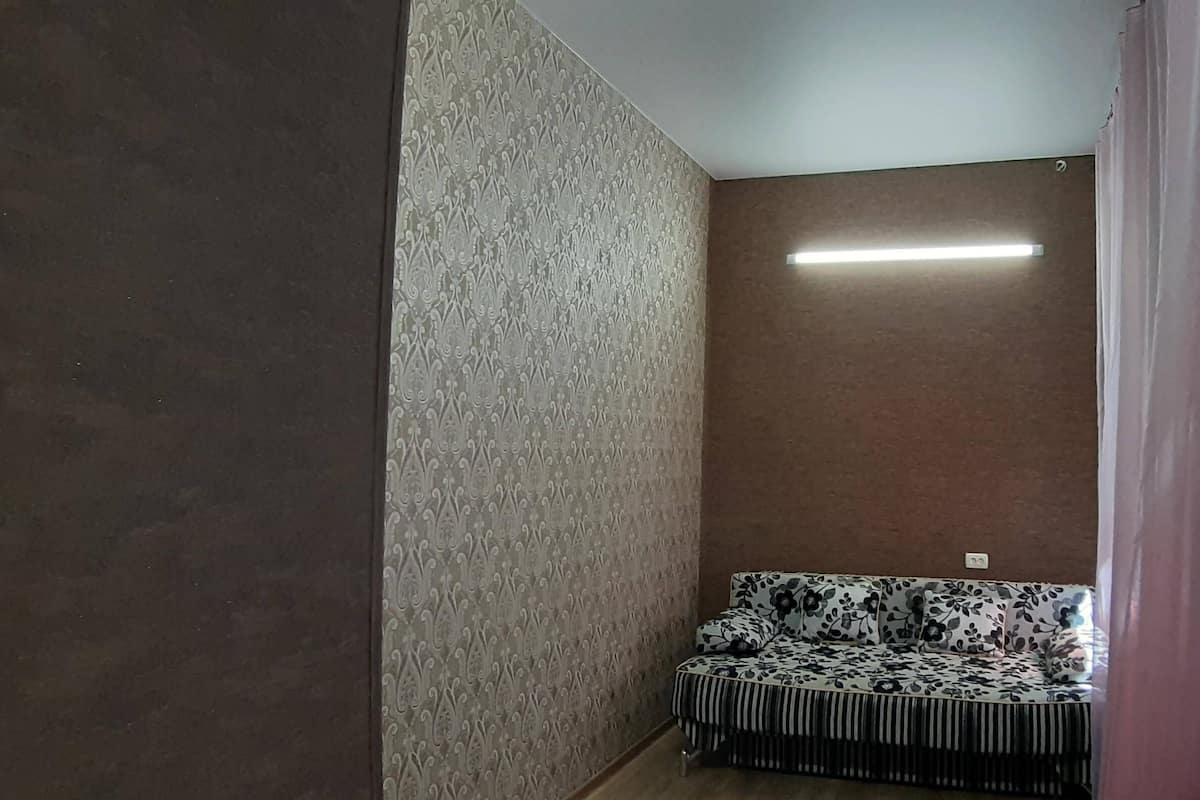 Una habitación de esquina con papel tapiz estampado, un sofá con tapicería floral y una lámpara de techo.