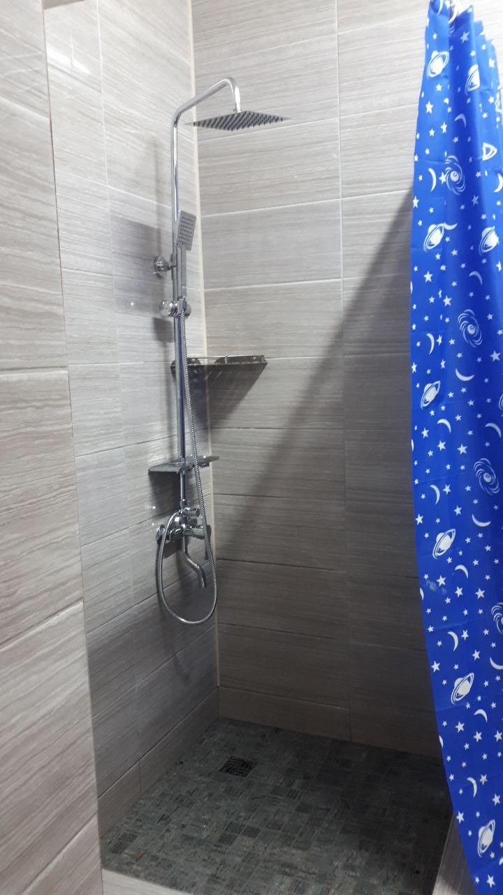 Una ducha con cabezal de ducha manual y un cabezal de ducha de lluvia empotrado, una cortina de baño azul con estampado de temática espacial, y un piso de baldosas.