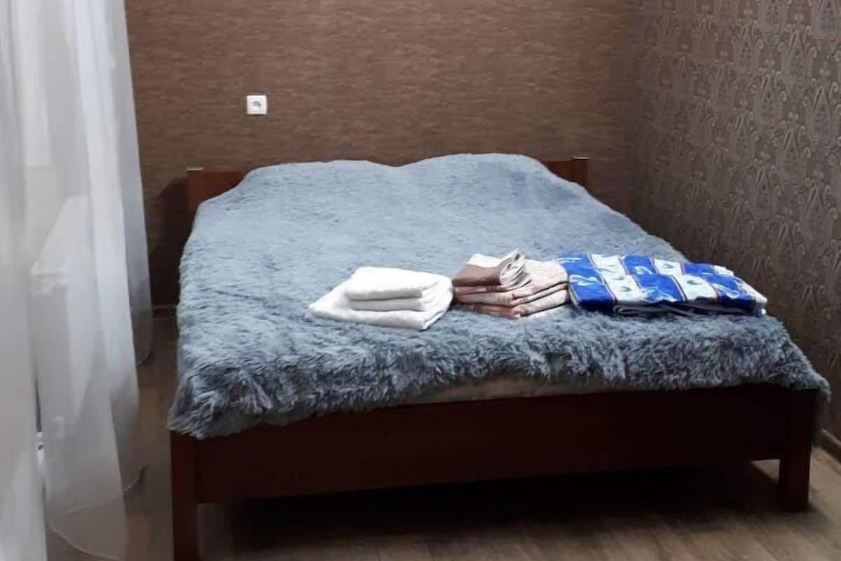 Una habitación pequeña y ordenada con una cama de madera, un papel tapiz estampado y una lámpara.