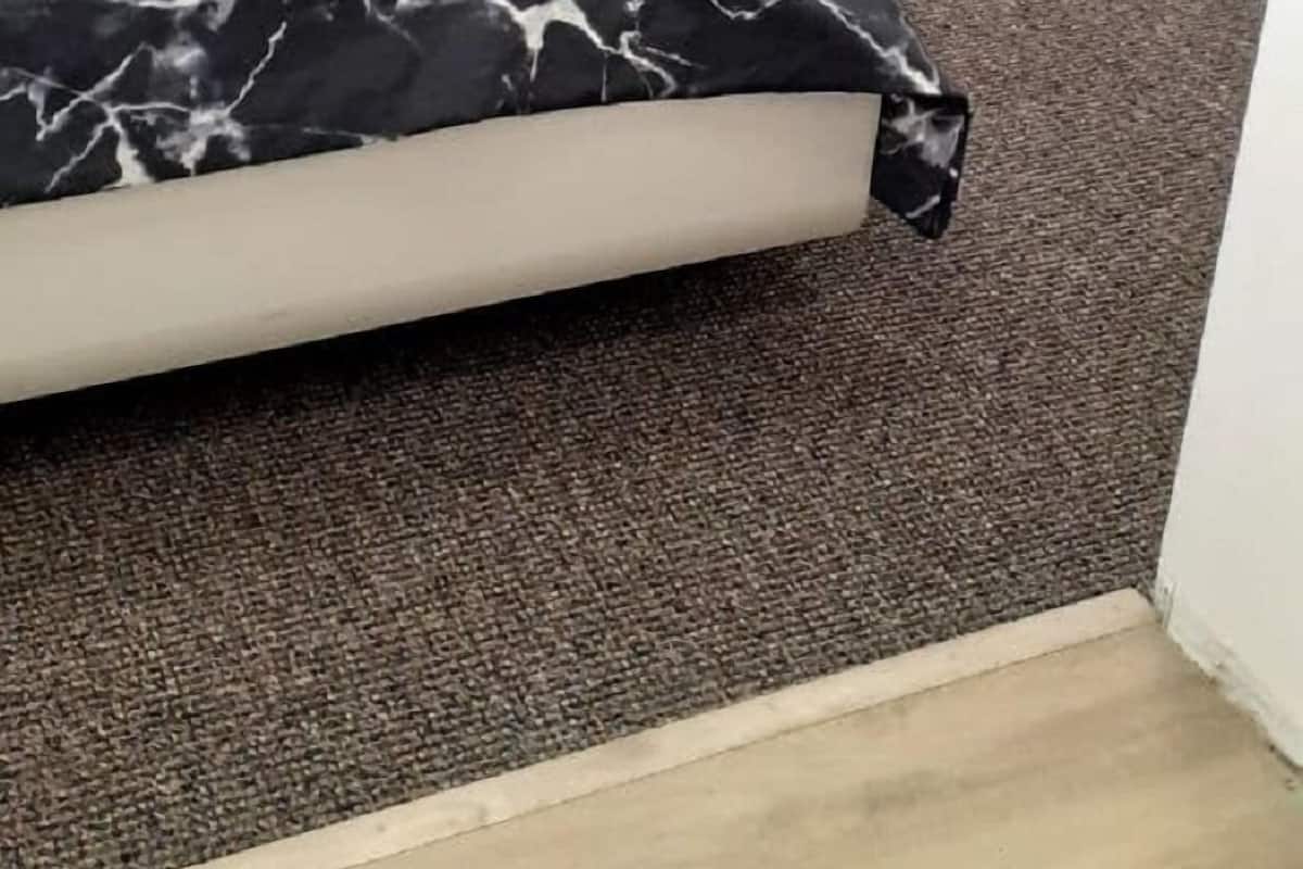 Un dormitorio con una cama, una silla, un tendedero y suelo alfombrado.