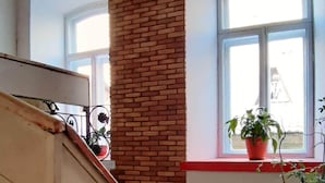 Una escalera con un columnilla de ladrillo, un rellano con tejas rojas y una planta en maceta sobre el rellano.