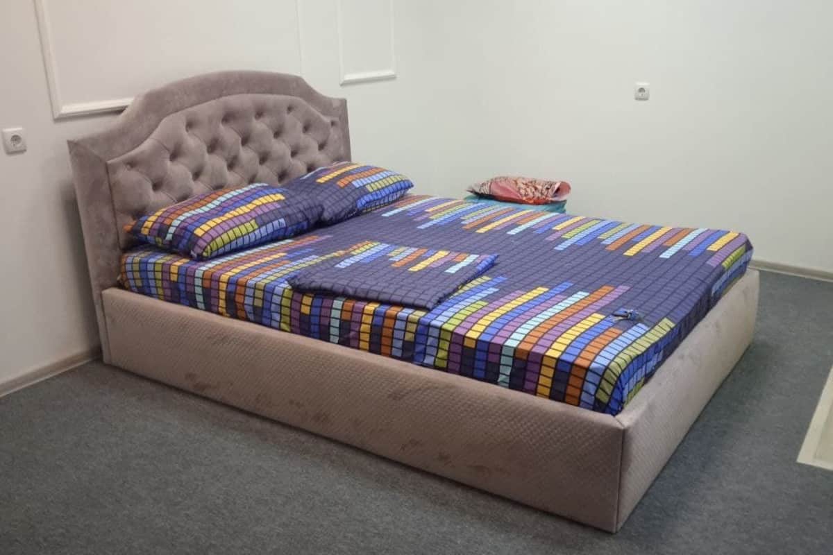 Una cama con cabecera capitonada, colcha colorida y una sola almohada.