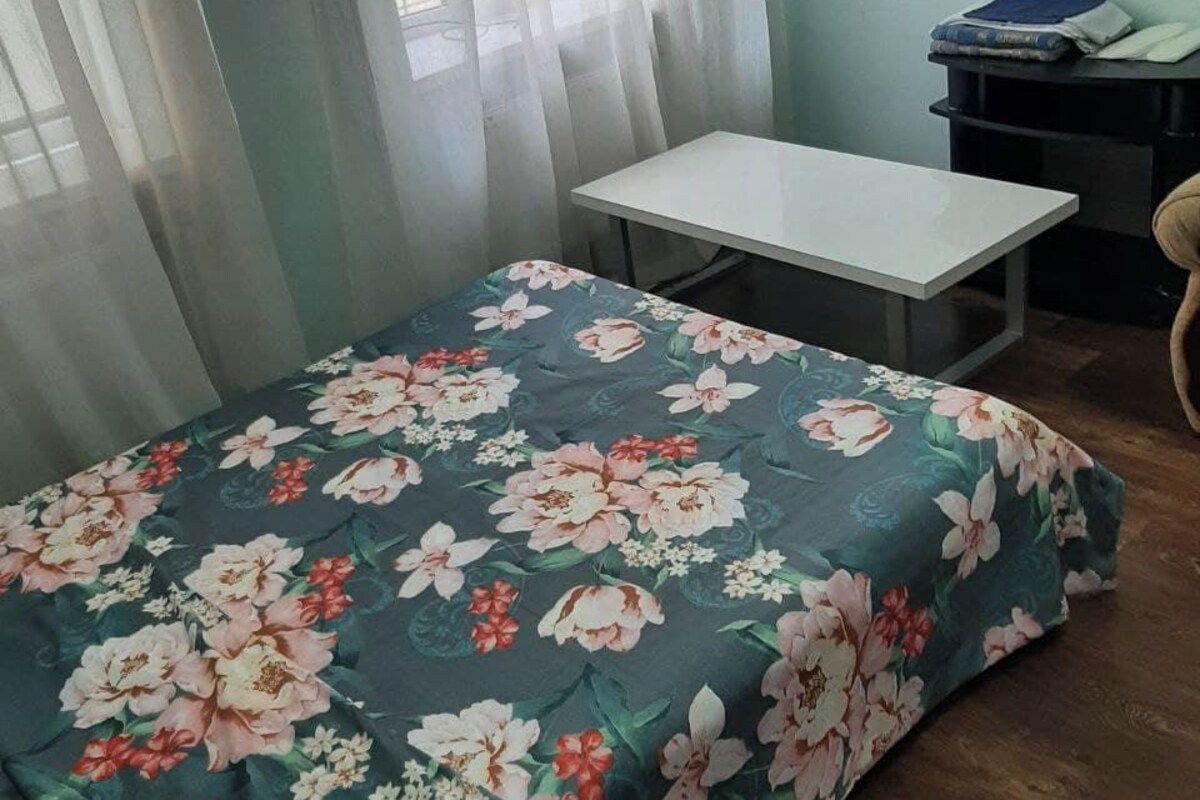 A bedroom with a bed, a small table, a chair, a TV on the wall, and a window with curtains.