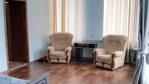Una habitación con piso de madera, dos sillones color beige, una mesita y una puerta.