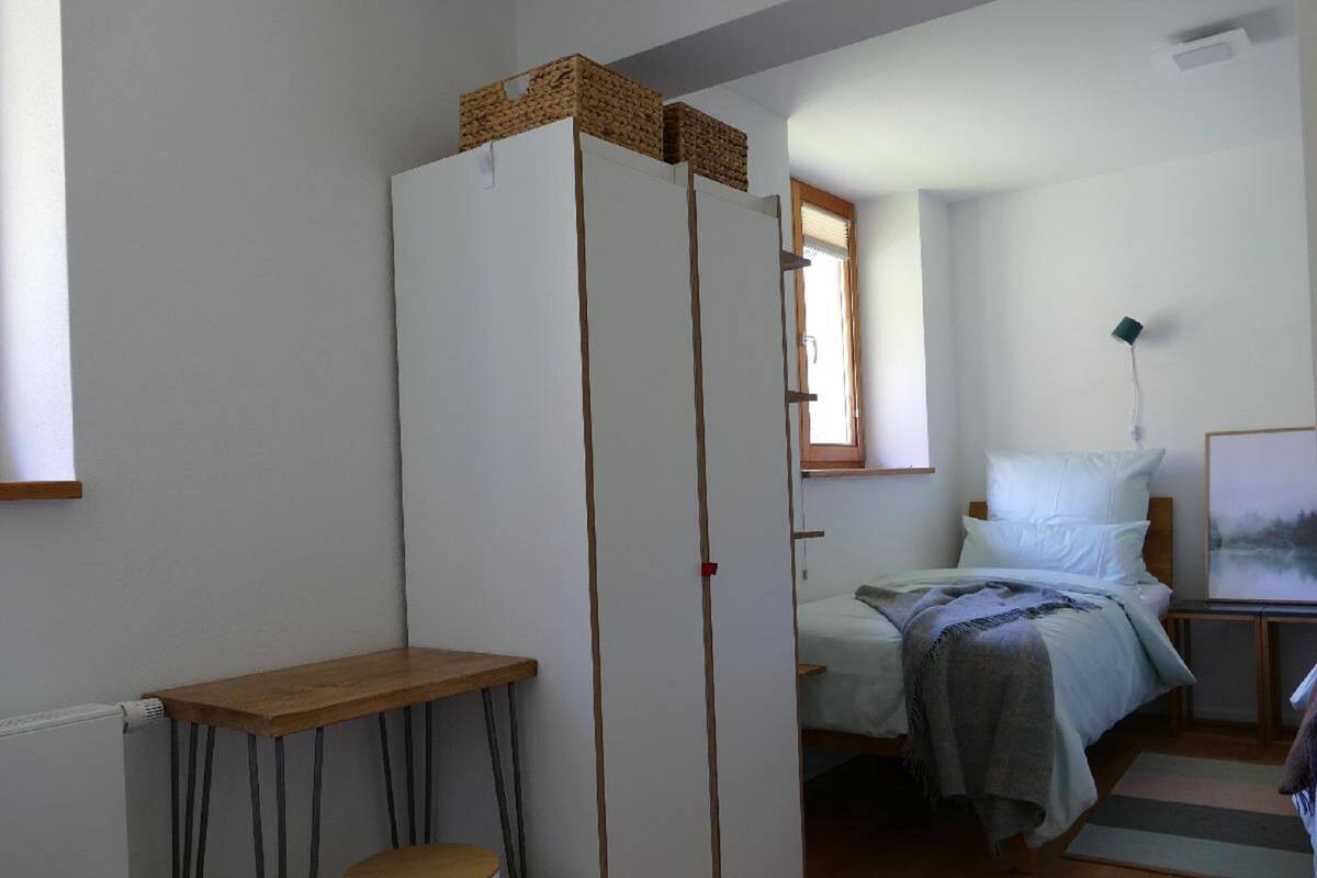 Pieni, käytännöllinen makuuhuone, jossa on yksi sänky, yöpöytä, puinen pöytä ja vaatekaappi.