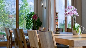 A dining area with wooden chairs and a table, a vase with flowers, and a potted plant. - Kraftquelle Waldhäuser (Neuschoenau)