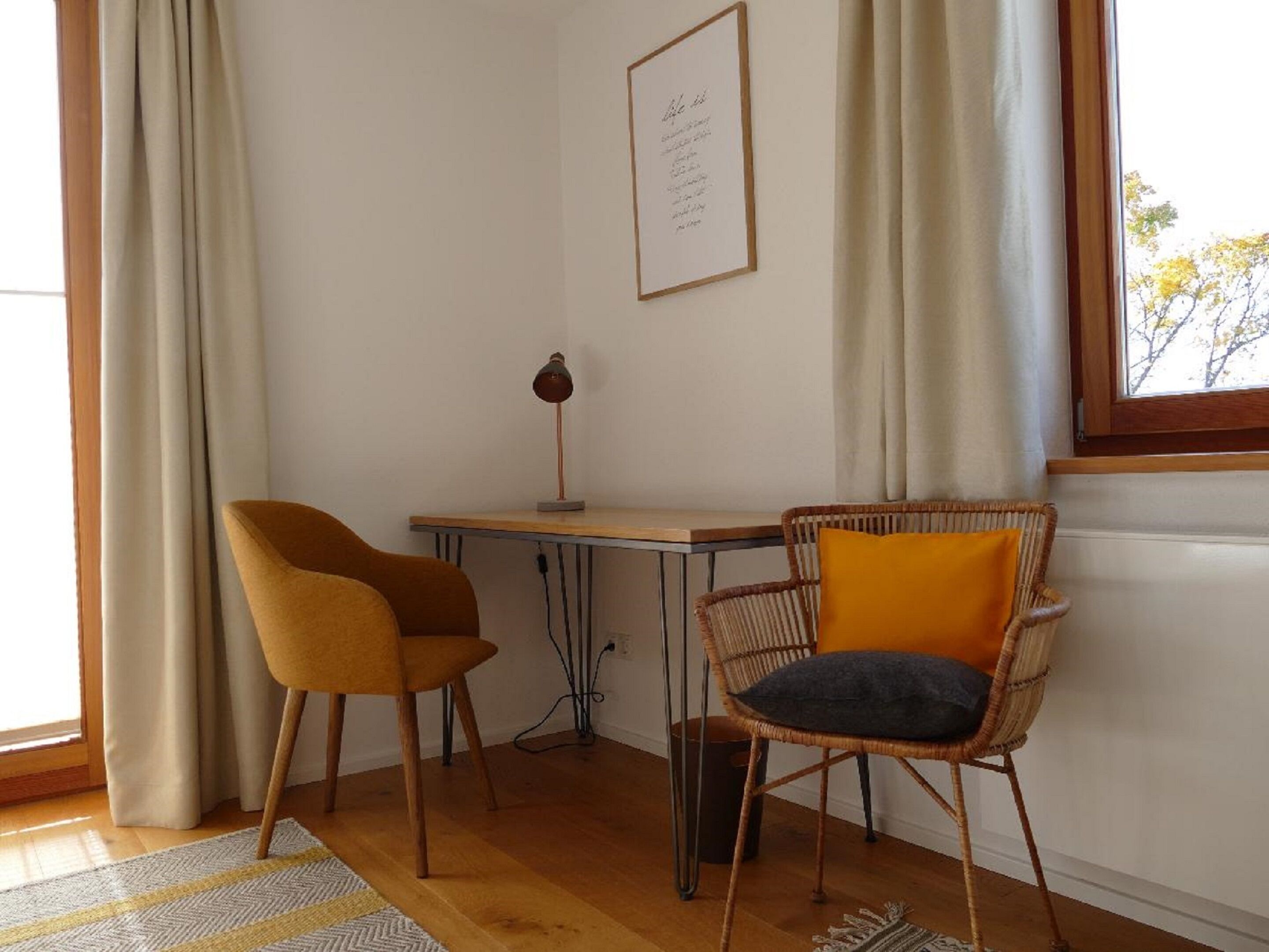 A room with a desk, two chairs, a lamp, and a window with curtains.