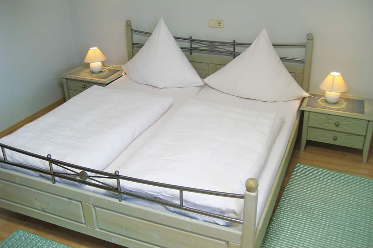 Una cama con dos camas individuales, ropa de cama blanca, dos mesitas de noche con lámparas y un tapete verde en el suelo.